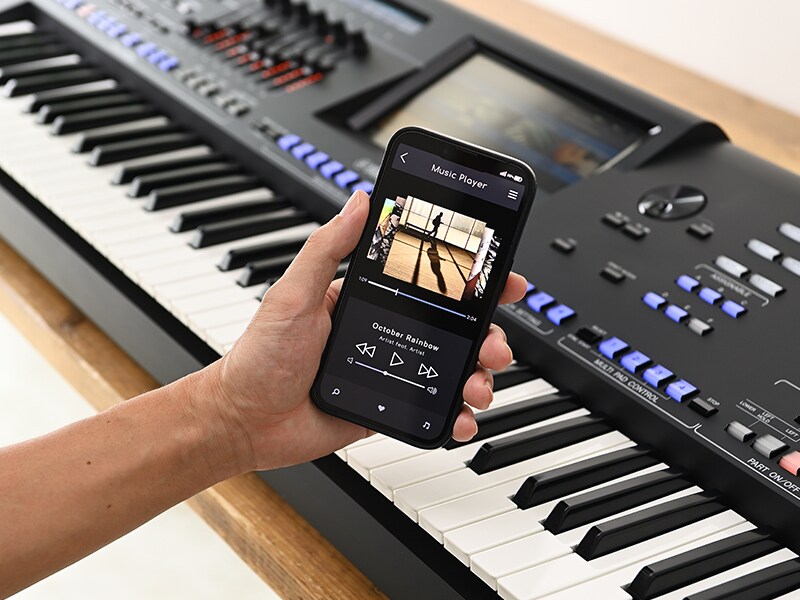 آلة جينوس 2 ويد تمسك بهاتف ذكي تظهر عليه شاشة مشغّل موسيقى