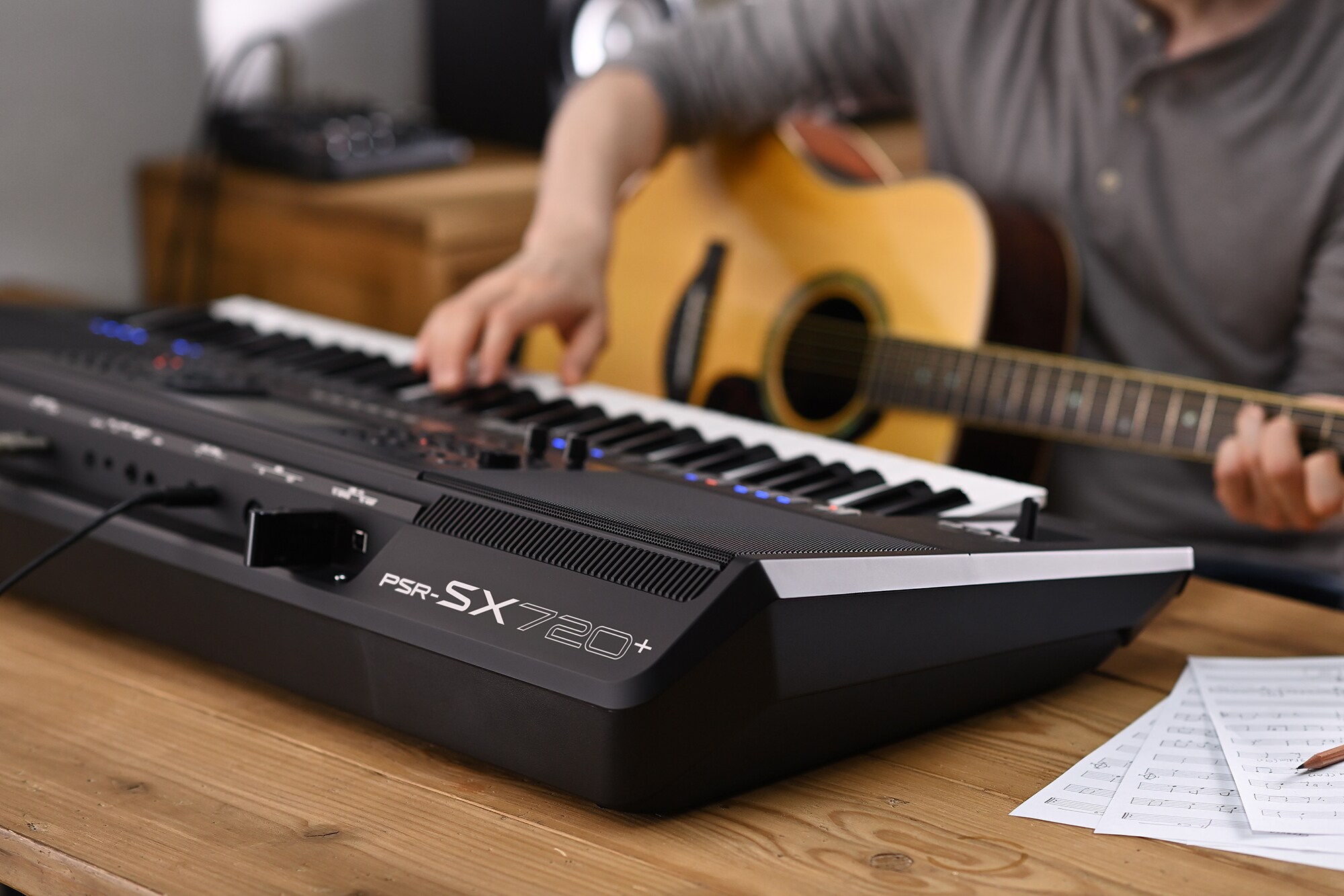 Photo of a person playing Yamaha Arranger Workstation PSR-SX720+ while holding a guitar